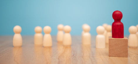 Red wooden figure standing in front of plain wooden figures